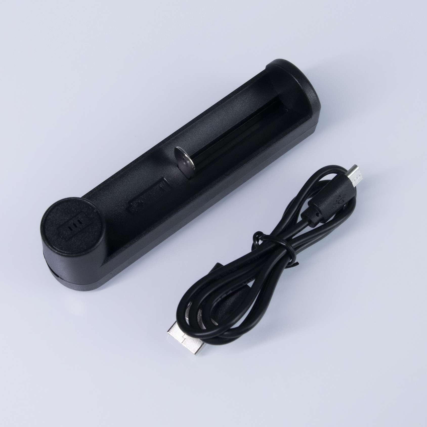 The same single-slot charger laid flat beside its coiled USB cable, showing the open slot and the spring contact at one end